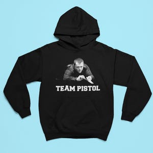 Puede incluir: Sudadera con capucha negra con un gráfico blanco de un hombre jugando al billar con el texto "TEAM PISTOL" debajo.