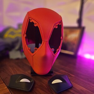May include: A red plastic mask with a textured surface and multiple holes. Two black plastic pieces with white accents are also shown.