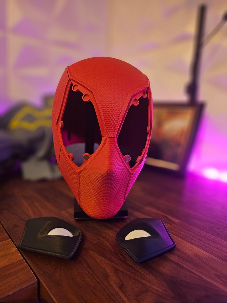 May include: A red plastic mask with a textured surface and multiple holes. Two black plastic pieces with white accents are also shown.
