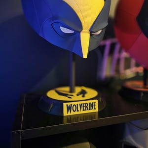 May include: A blue and yellow Wolverine mask on a black stand with a yellow base that says "Wolverine".