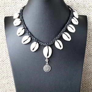 May include: A black cord necklace with white shell charms and a silver pendant featuring a scale symbol.
