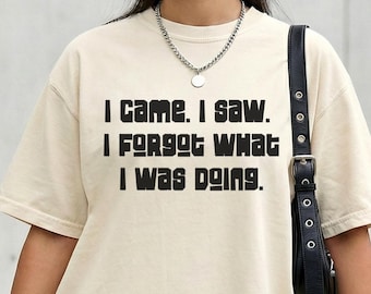 May include: Cream-colored t-shirt with the text "I came. I saw. I forgot what I was doing." in black block letters. The shirt has short sleeves and a relaxed fit.