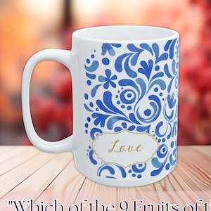 Op de afbeelding: Witte keramische mok met een blauw bloemmotief en het woord "Love" in een gouden kader. De mok heeft een gebogen oor en de tekst "Which of the 9 Fruits of the Spirit speaks to you?" staat onderaan.