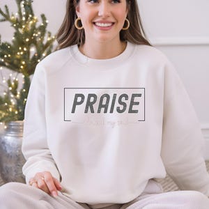 Puede incluir: Sudadera blanca con el texto "PRAISE the Lord my soul" en letras negras y rosas.