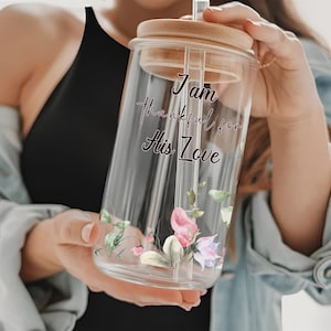 Puede incluir: Un vaso de vidrio transparente con tapa y pajita de bambú. El vaso está decorado con diseños florales y el texto "I am thankful for His Love".