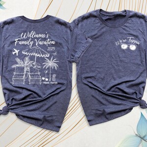 Pode incluir: Duas camisetas azul marinho. Uma camiseta apresenta o texto "Williams's Family Vacation 2025 Miami, Florida" com um gr&aacute;fico de cena de praia. A outra camiseta tem o texto "We're Trippin" com &oacute;culos de sol. Ambas as camisetas t&ecirc;m mangas curtas.