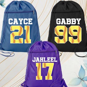 May include: Three drawstring sports bags in blue, black, and purple. Each bag features a name and number in white and yellow, with a baseball design. The blue bag says "CAYCE 21", the black bag says "GABBY 99", and the purple bag says "JAHLEEL 17".