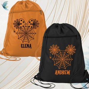 May include: Two drawstring backpacks, one orange and one black, featuring Halloween-themed designs. The orange bag has a bow and spiderweb design with the name "ELENA". The black bag has a Mickey Mouse-inspired spiderweb design with the name "ANDREW".