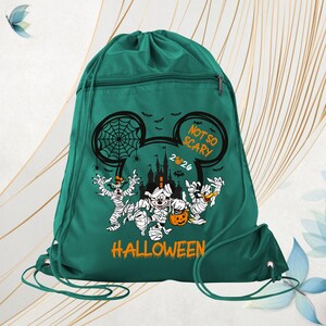 May include: A dark green drawstring backpack featuring a graphic of cartoon characters dressed as mummies. The design includes a castle silhouette, spiderwebs, bats, and the text "NOT SO SCARY 2024 HALLOWEEN" printed in orange and white.