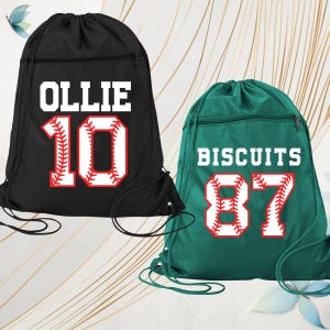 May include: Two drawstring backpacks. One is black with the name "OLLIE" and the number "10" in a baseball-style font. The other is green with the name "BISCUITS" and the number "87" in a baseball-style font. Both have a zippered pocket.