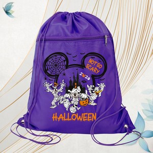 May include: A purple drawstring backpack featuring a graphic of Disney characters dressed as mummies. The design includes a castle silhouette, spiderwebs, bats, and the text "NOT SO SCARY 2024 HALLOWEEN" in orange and white lettering.