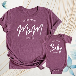 May include: Burgundy t-shirt and baby bodysuit set. The adult shirt features the word "Mom" with "Reyes Family" above and "Est. 2026" below. The baby bodysuit says "Baby" with "Reyes Family" above and "Est. 2026" below.
