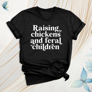 Peut inclure: T-shirt noir avec un texte blanc qui dit "&Eacute;lever des poulets et des enfants sauvages".