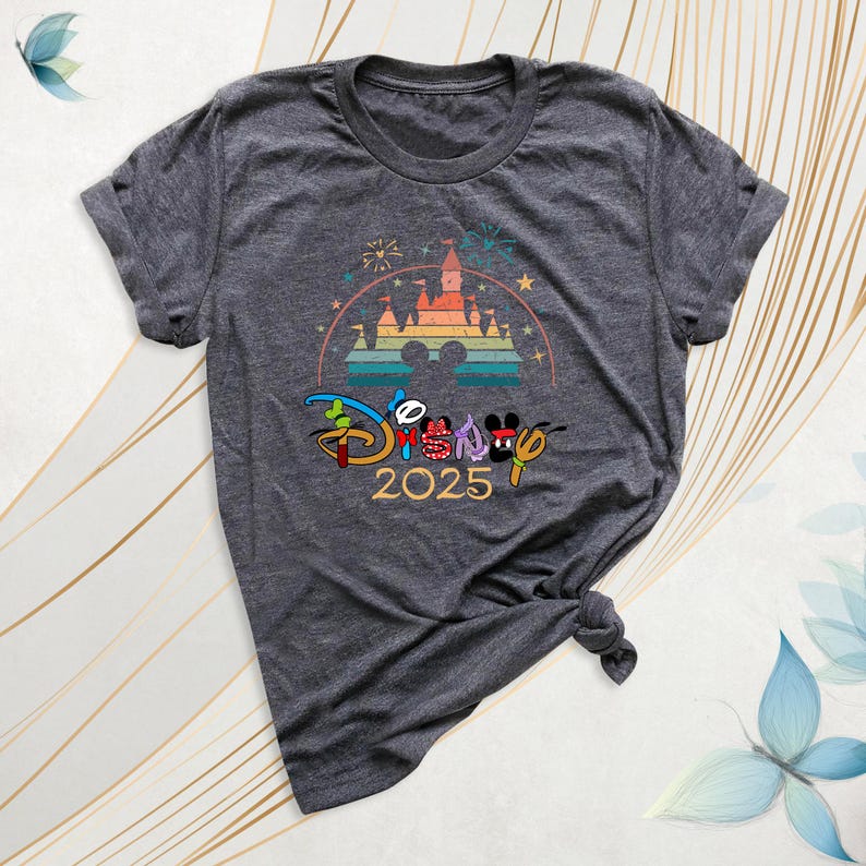 May include: Dark gray t-shirt featuring a colorful Disney design. The design includes a castle, fireworks, and the text "Disney 2025" with Mickey and Minnie Mouse. The shirt is knotted at the bottom.