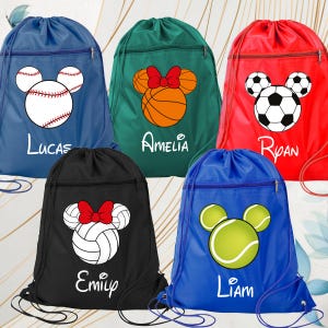 May include: Five drawstring backpacks in blue, green, red, black, and blue. Each bag features a front zipper pocket and a graphic of a sports ball shaped like a mouse head with a name printed below: Lucas, Amelia, Ryan, Emily, and Liam.