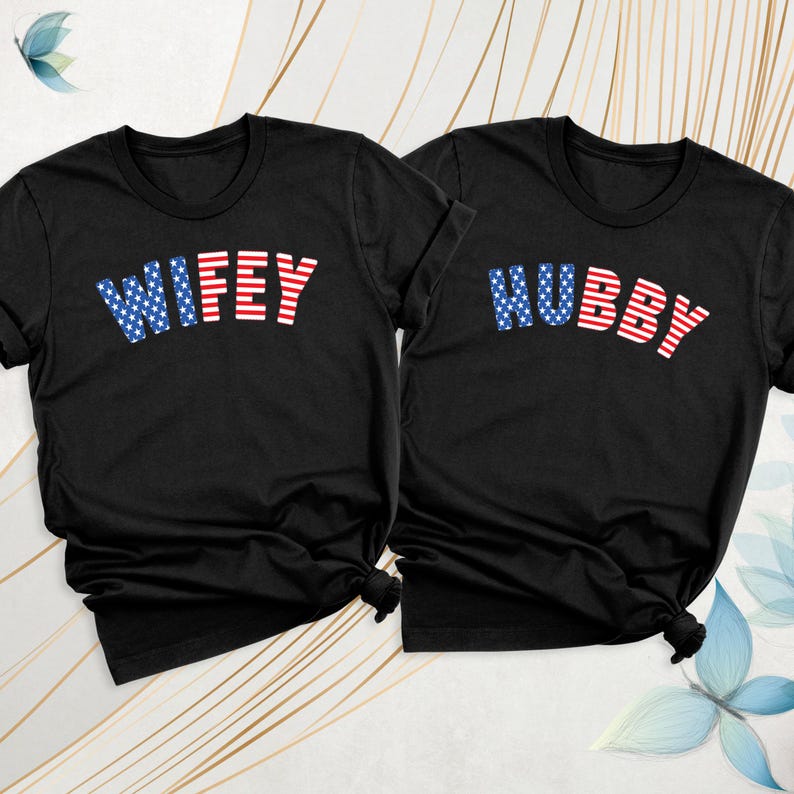 Puede incluir: Dos camisetas negras con las palabras "WIFEY" y "HUBBY" impresas. El texto est&aacute; en rayas rojas y blancas con un patr&oacute;n de estrellas azules. Las camisetas son probablemente para parejas.