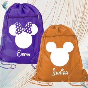 May include: Two drawstring bags, one purple and one orange. The purple bag features a white Minnie Mouse design with a polka dot bow and the name "Emma". The orange bag has a white Mickey Mouse design and the name "Junior". Both bags have a zipped pocket.