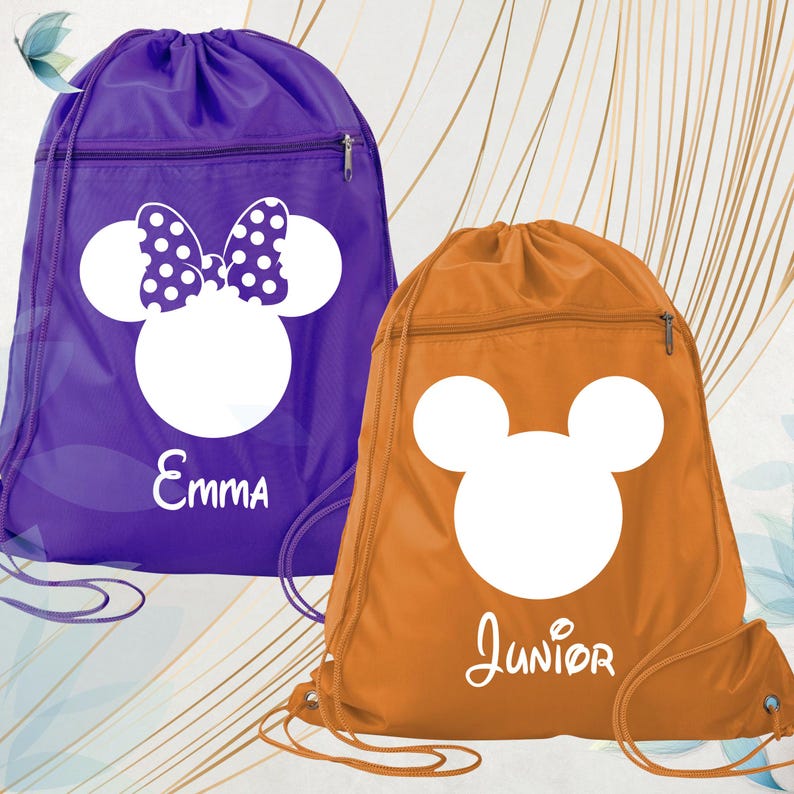May include: Two drawstring bags, one purple and one orange. The purple bag features a white Minnie Mouse design with a polka dot bow and the name "Emma". The orange bag has a white Mickey Mouse design and the name "Junior". Both bags have a zipped pocket.
