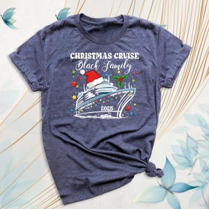 May include: A heather navy blue t-shirt featuring a graphic of a cruise ship wearing a Santa hat. The text reads CHRISTMAS CRUISE Black Family 2025. The design includes colorful holiday ornaments and holly leaves surrounding the ship.