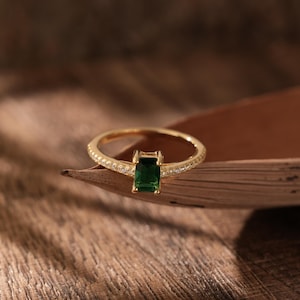 May include: A gold ring featuring a green emerald gemstone, surrounded by smaller clear stones on the band.