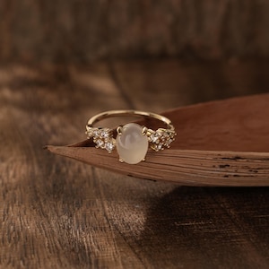 May include: A gold ring featuring a white oval gemstone and small clear stones set in a leaf-like design.
