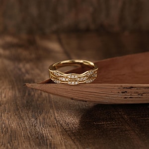 May include: A gold ring with three bands of diamonds set in a wavy pattern. The ring is resting on a piece of wood.