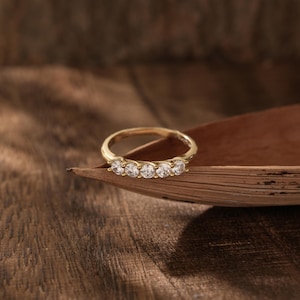 May include: A gold band ring with five clear round stones set in a row.