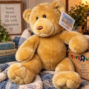 May include: A golden-brown plush teddy bear with dark eyes and a brown stitched nose. A white rectangular tag attached to the ear reads Animal Alley Only at Toys R Us. The bear has soft fur, rounded ears, and a seated posture with visible paw pads.