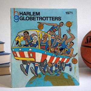 Könnte beinhalten: Vintage Buchcover der Harlem Globetrotters von 1971 mit einer Cartoon-Illustration des Teams in einem Bus. Rechts ist ein Basketball. Das Cover ist hellblau mit dem Teamnamen und dem Jahr.