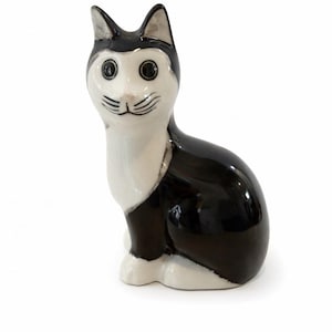 May include: A ceramic cat ornament in a seated pose. The cat is predominantly black and white, featuring black ears and a black head marking. The face is white with black eyes and whiskers.