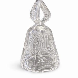 May include: Clear glass bell with a decorative handle. The bell features intricate floral and geometric patterns. The bell is transparent, allowing light to pass through, and sits on a white background. The bell is likely a decorative item.
