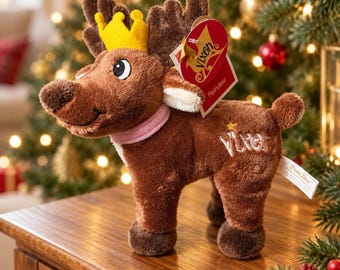 May include: A brown plush reindeer toy wearing a yellow felt crown and a light pink collar. The reindeer features dark brown antlers, embroidered eyes, and the name Vixen stitched in white thread on its side with a small yellow star above it.