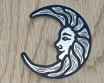 May include: A black and white sticker of a crescent moon with a stylized human face inside. The face has a long, flowing mane of hair.