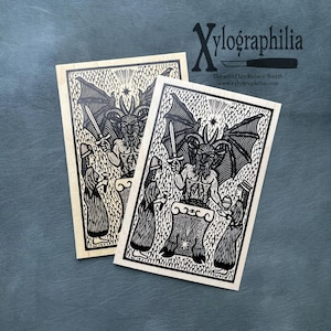 May include: Two black and white art prints featuring a detailed illustration of a horned figure holding a sword, surrounded by other figures. The prints are on a cream-colored background. The text "Xylographilia" is at the top.