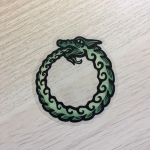 May include: A green and black sticker of a dragon curled into a circle, forming an ouroboros symbol.