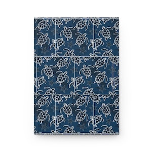 May include: A notebook with a navy blue cover featuring a white, repeating pattern of sea turtles and starfish. The design is arranged in a grid-like fashion, with white lines separating the pattern. The notebook is rectangular and appears to be closed.