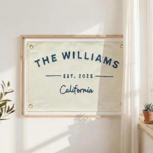 Könnte beinhalten: Ein gerahmtes Wandbild aus Leinwand mit dem Text "THE WILLIAMS" über "EST. 2025" und "California" in Marineblau. Die Leinwand ist hellbeige und der Rahmen aus hellem Holz.