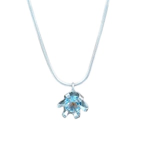May include: A silver chain necklace with a blue gemstone pendant. The pendant is a flower shape with a single blue gemstone in the center.