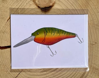May include: A colorful watercolor illustration of a fishing lure. The lure features a long, silver bill, a green and yellow top, and a red and orange body. Two silver hooks are attached to the bottom.