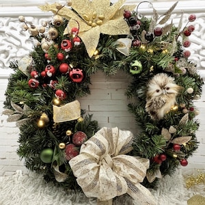 Pode incluir: Uma coroa de Natal com uma coruja marrom, bagas vermelhas, uma poinsétia dourada com glitter e um laço bege com glitter dourado.