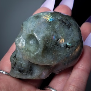 以下が含まれることがあります： 虹色の虹色の光沢を持つ緑色のラブラドライトクリスタル製の頭蓋骨。頭蓋骨は天然石から彫られており、滑らかで磨かれた仕上げになっています。