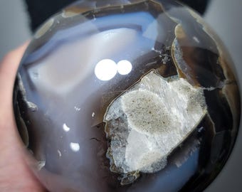 Peut inclure: Une sphère d'agate polie avec un motif de bandes blanches, grises et noires. La sphère a une finition lisse et brillante et est une pierre naturelle.