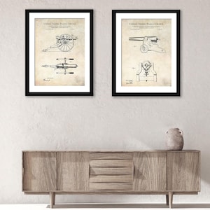 May include: Two framed vintage patent drawings of cannons. The drawings are in black and white and have a beige background. The text "United States Patent Office" is visible at the top of each drawing.