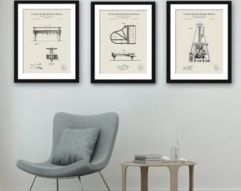 May include: Three black framed prints with white backgrounds and black text. The prints are of vintage patent drawings for a piano, a piano, and a drilling rig. The prints are hanging on a white wall above a gray chair and a wooden table.