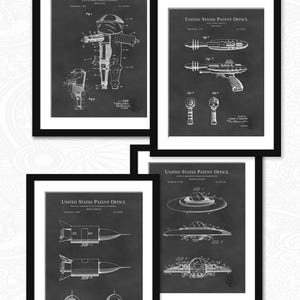 May include: Four black and white framed prints of vintage patent drawings for a space suit, ray gun, flying saucer, and rocket ship. The drawings are on a dark gray background with white lines and text. The text includes "United States Patent Office" and the patent number.