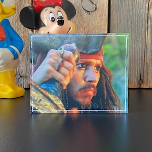 May include: A close-up of Jack Sparrow, a fictional character from the Pirates of the Caribbean film series. He is wearing a red bandana and has long, dark hair. He is holding a sword in his right hand and looking off to the side.