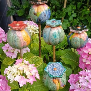 Può includere: Cinque picchetti da giardino in ceramica con corpi arrotondati a forma di zucca e smalti screpolati multicolori nelle tonalità del blu, verde, arancione e rosa. Ogni picchetto è sormontato da un tappo piatto a forma di fiore su un'asta.