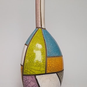 Könnte beinhalten: Eine farbenfrohe Keramikvase mit einem geometrischen Patchwork-Design. Die Vase hat einen schlanken Hals und einen bauchigen Körper mit Abschnitten in Blau, Gelb, Orange, Lila und Weiß. Die Oberfläche hat einen Craquelé-Effekt.