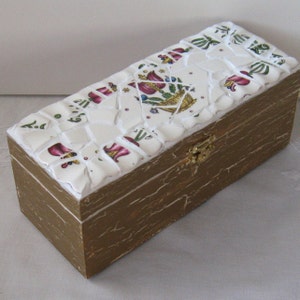 May include: A white wooden box with a mosaic tile design featuring floral patterns in shades of pink, green, and white. The box has a gold-painted finish and a brass latch.