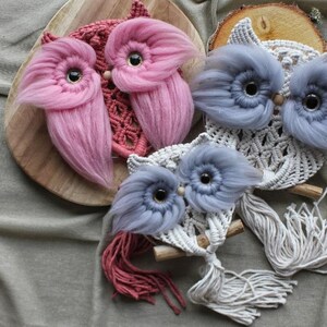 May include: Three handmade macrame owl wall hangings with fringe. The owls are in shades of pink, blue, and white.